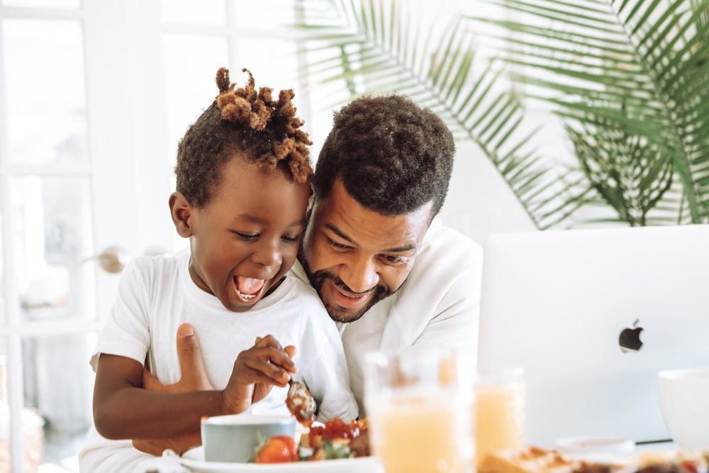 Joyful father and child sharing a light moment during breakfast.