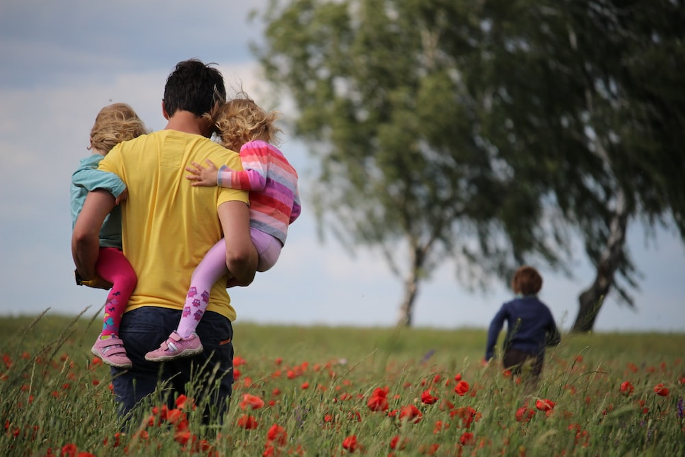 A father playing with his children in a field of flowers. 