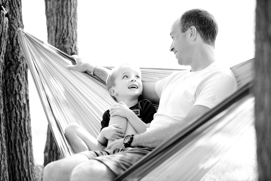 A happy parent and child in a hammock by https://www.pexels.com/photo/grayscale-photo-of-man-and-child-sitting-on-hammock-208106/