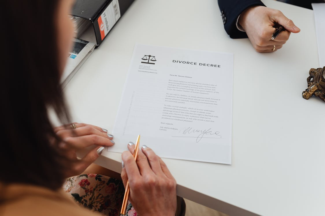 A woman signing a divorce decree by https://www.pexels.com/photo/a-woman-reading-a-divorce-decree-paper-7876044/