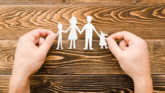 Hands holding a paper cutout of a family by https://www.freepik.com/free-photo/creative-arrangement-family-concept-wooden-background_7405131.htm#fromView=search&page=1&position=5&uuid=d3cd5ac8-a3b0-4eae-9f67-ee24eff1154b