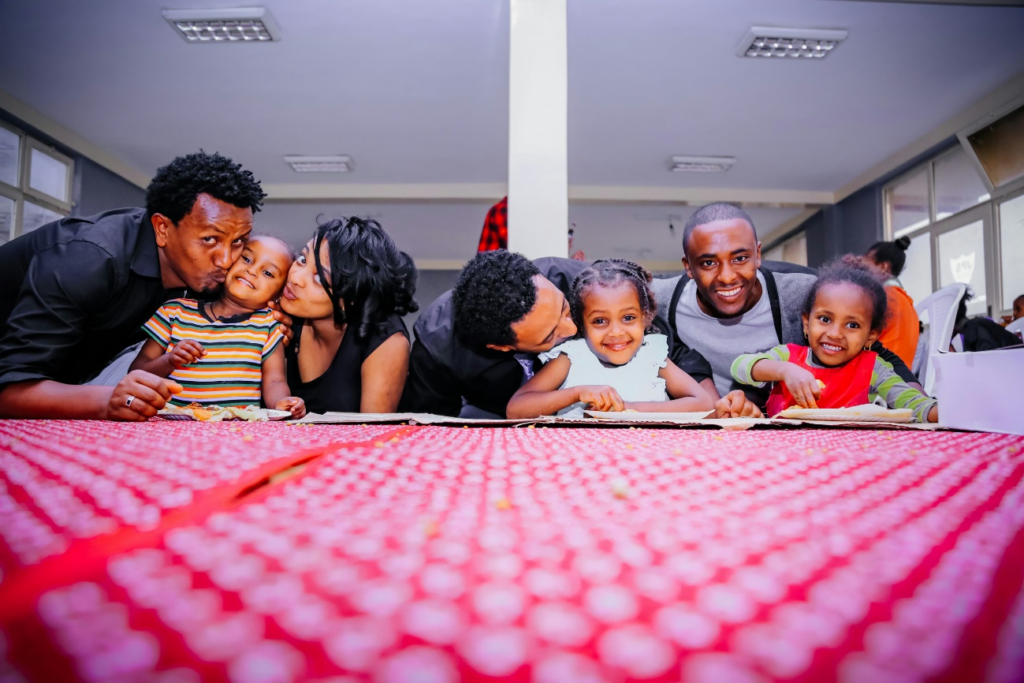 A happy family of parents and children enjoying a gathering together. by https://unsplash.com/photos/woman-and-three-men-with-three-children-on-front-of-desk-with-red-cloth-44XRowmXF24