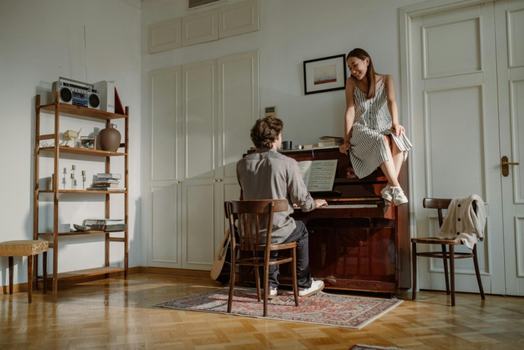 A woman sits on a piano while a man plays it